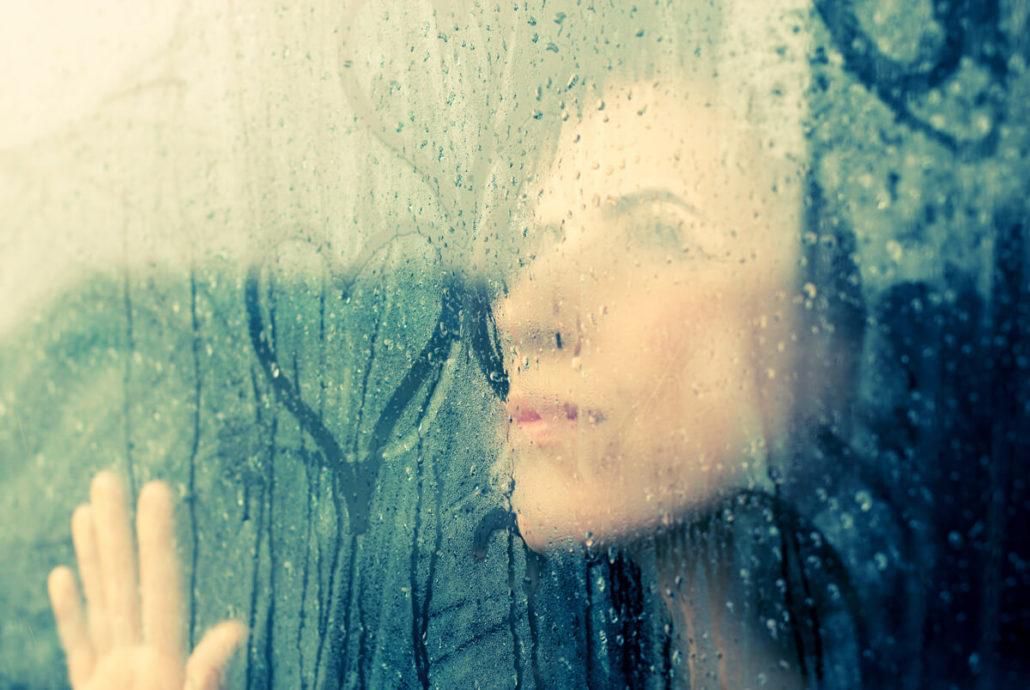 Mujer pensativa tras una ventana con lluvia